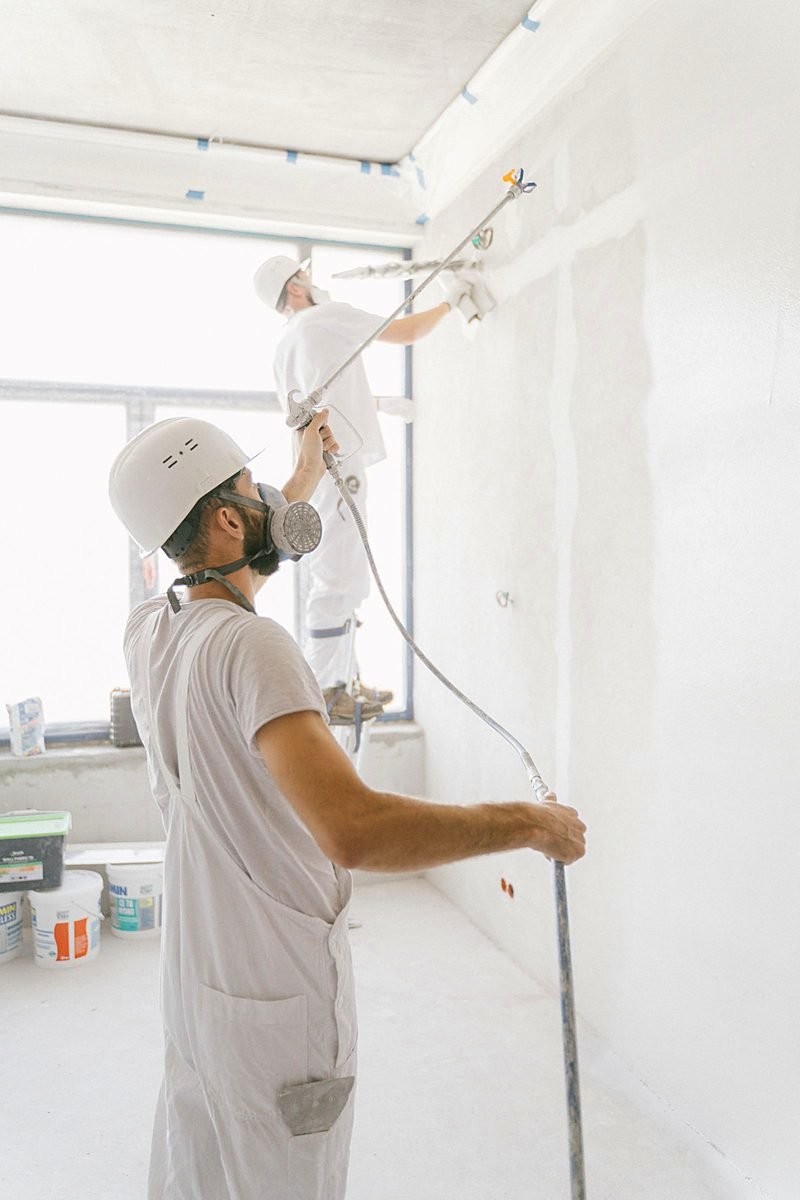 Two DDP painters in whites and hard hats spray finishing a commercial interior