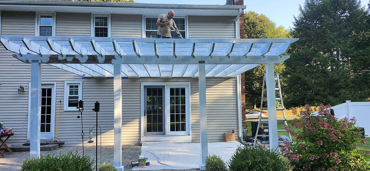 A DDP painter finishing a backyard pergola in bright white